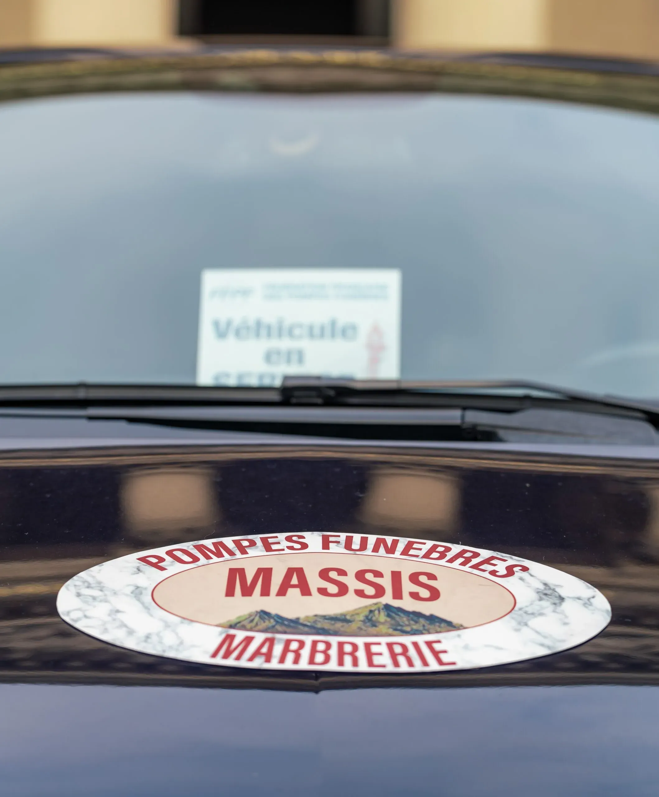 Gros plan sur le logo Massis et la mention "véhicule en service" sur un corbillard.